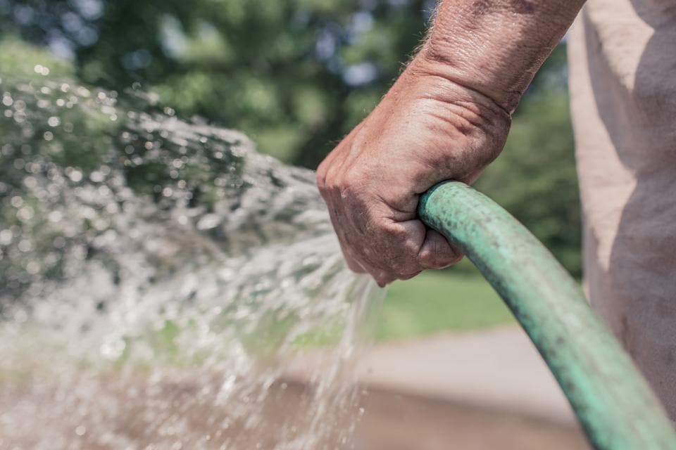 Hand am Gartenschlauch, Wasser spritzt beim Gießen
